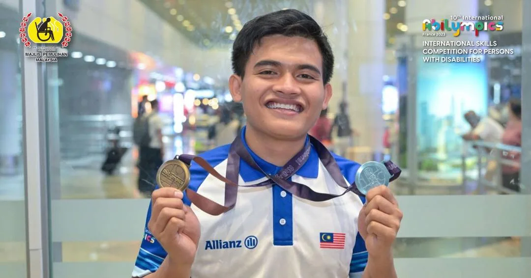 A Malaysian Abilympian smiles at the airport holding two medals on the team's return from the 10th International Abilympics in Metz.