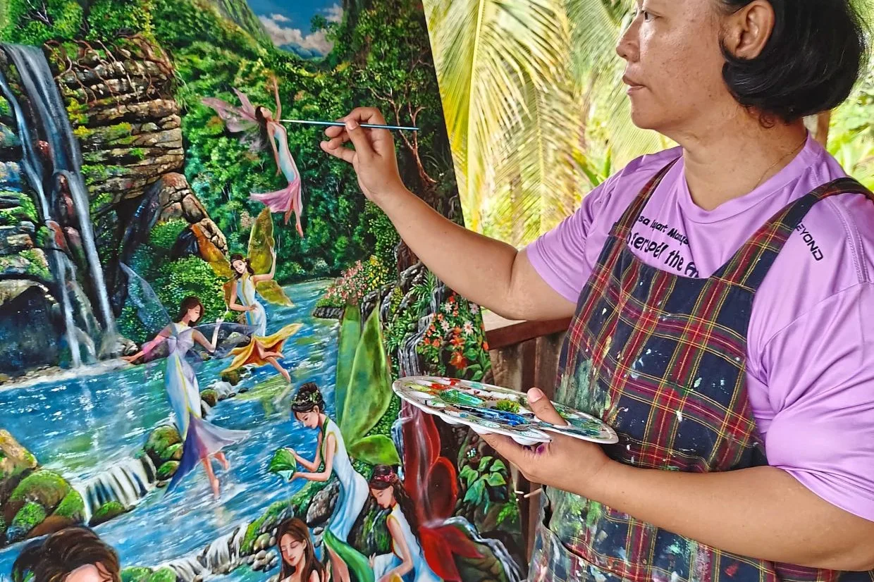 Rosemary Yvonne Marcus painting a tropical waterfall mural in Telupid, Sabah.