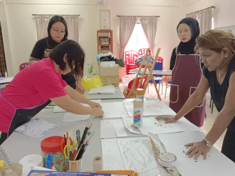 Trainees and trainers working over sketches and painting materials at a Painting & Waste Reuse training workshop.