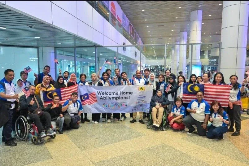 Team Malaysia's Abilympians and supporters with Malaysian flags at the airport, welcomed home from the 10th International Abilympics.